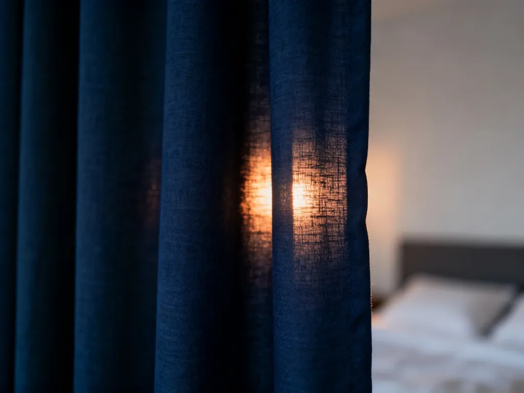 Zbliżenie na gęstą, granatową tkaninę typu blackout, która skutecznie blokuje światło słoneczne w sypialni.